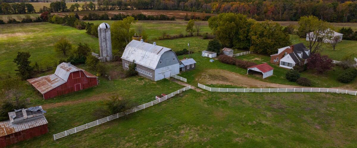 A rural farm with barns, a silo, and a white fence.