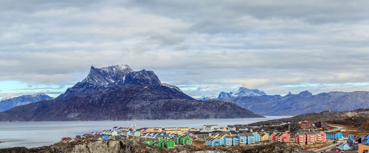 Un borgo costiero con case colorate, una montagna imponente e un mare calmo.
