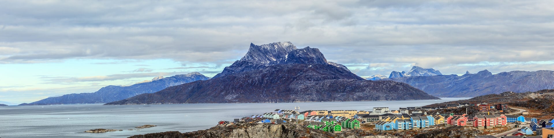 A coastal town with colorful houses, a prominent mountain peak, and a calm sea.