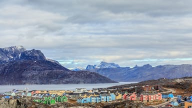 Un pueblo costero con casas coloridas, un pico montañoso destacado y un mar tranquilo.