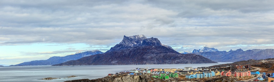 A coastal town with colorful houses, a prominent mountain peak, and a calm sea.