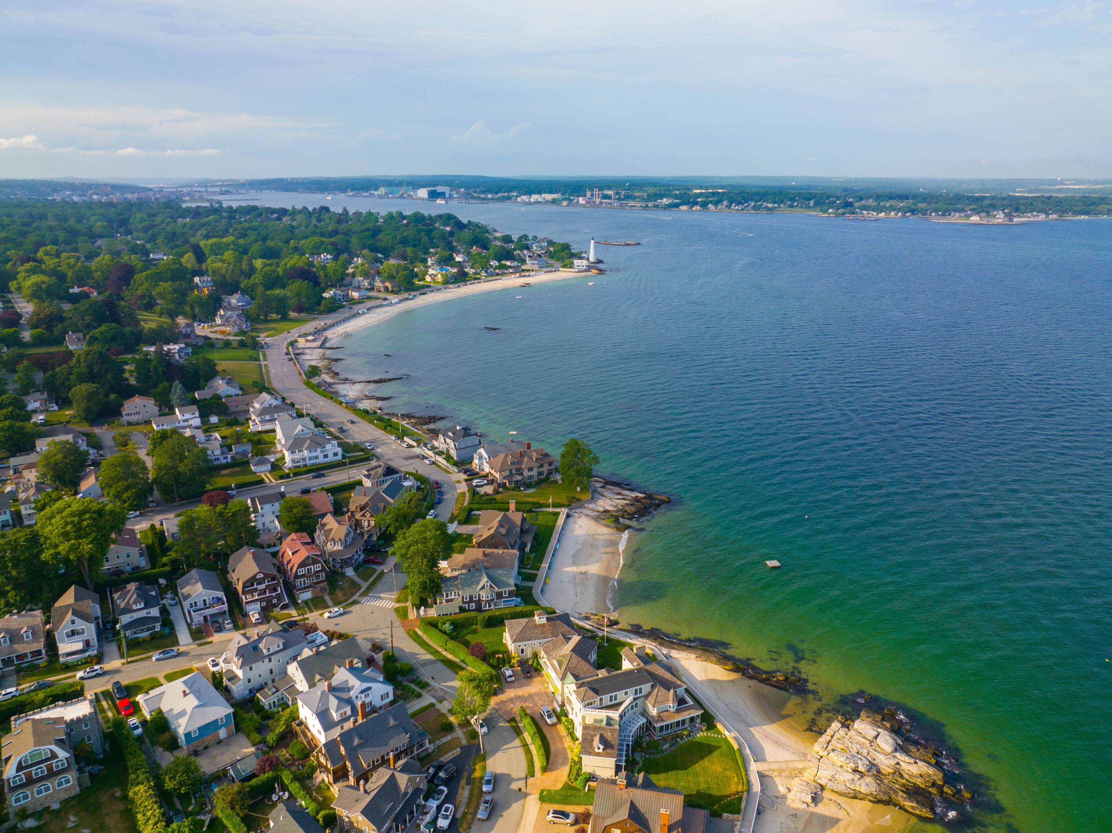 A coastal town with a beach, houses, and a lighthouse.