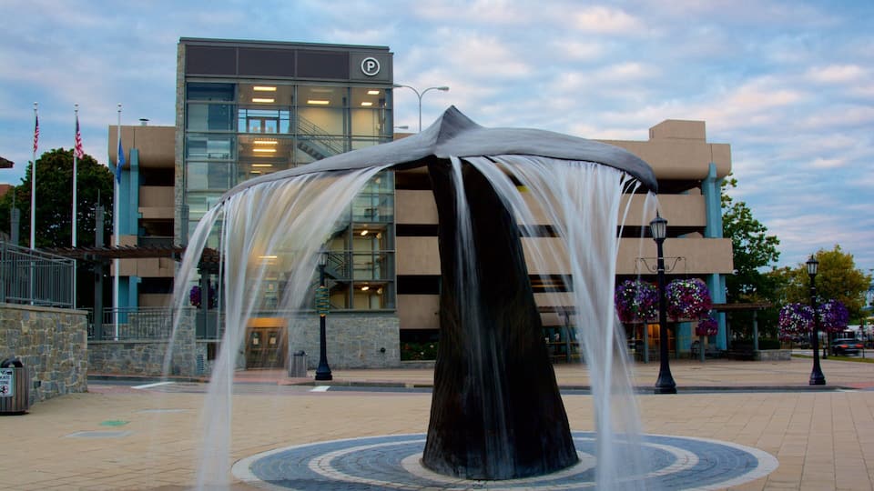 A modern building with a parking sign, a fountain sculpture, and a landscaped area with flowers.