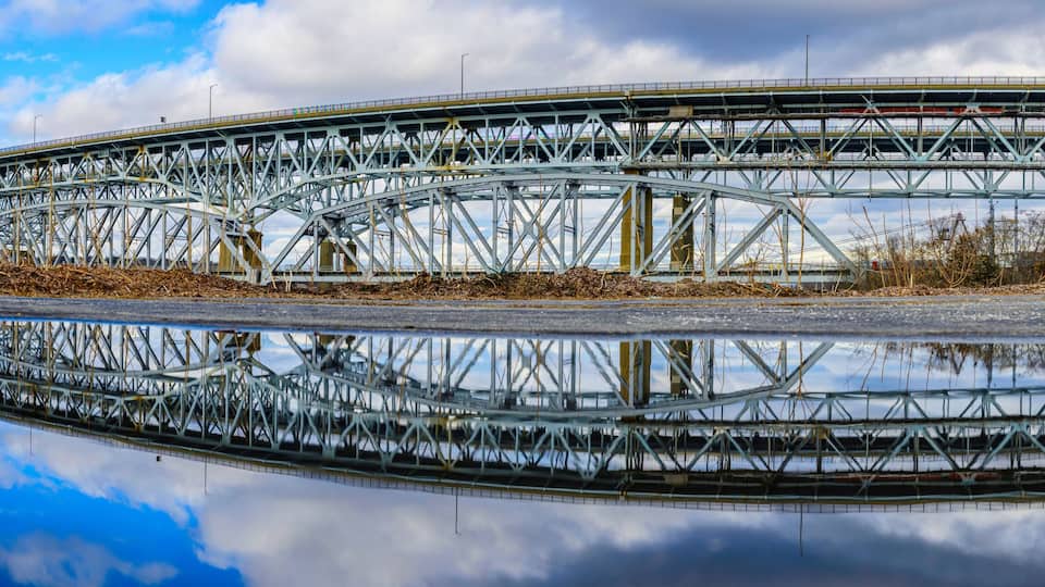 A large steel bridge with a clear reflection in the water below.
