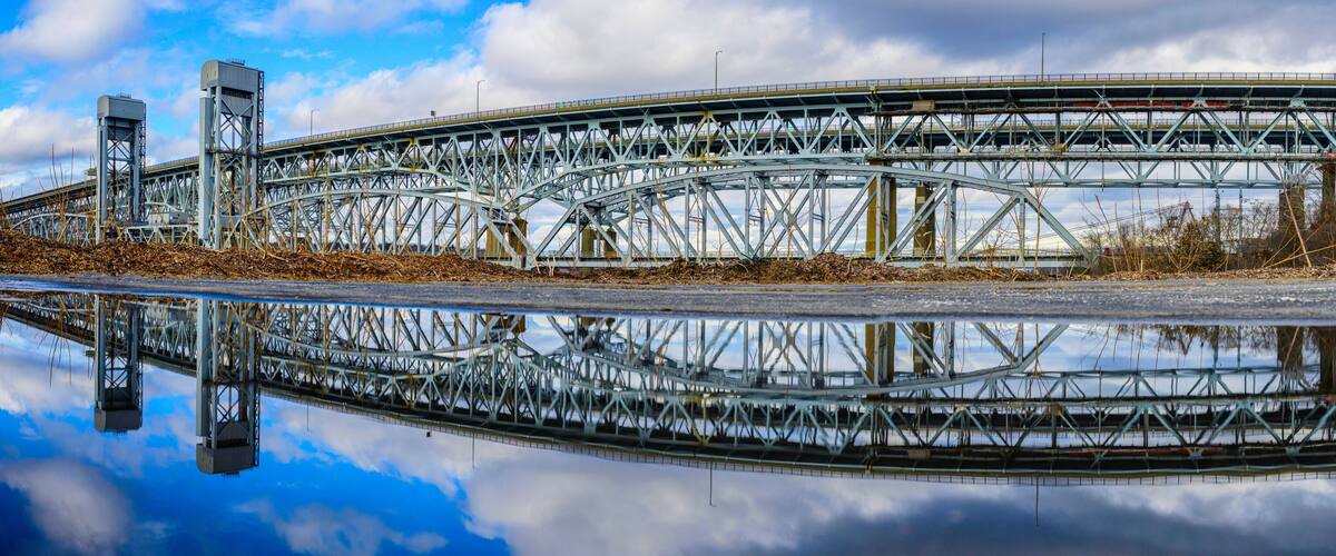A large steel bridge with a clear reflection in the water below.
