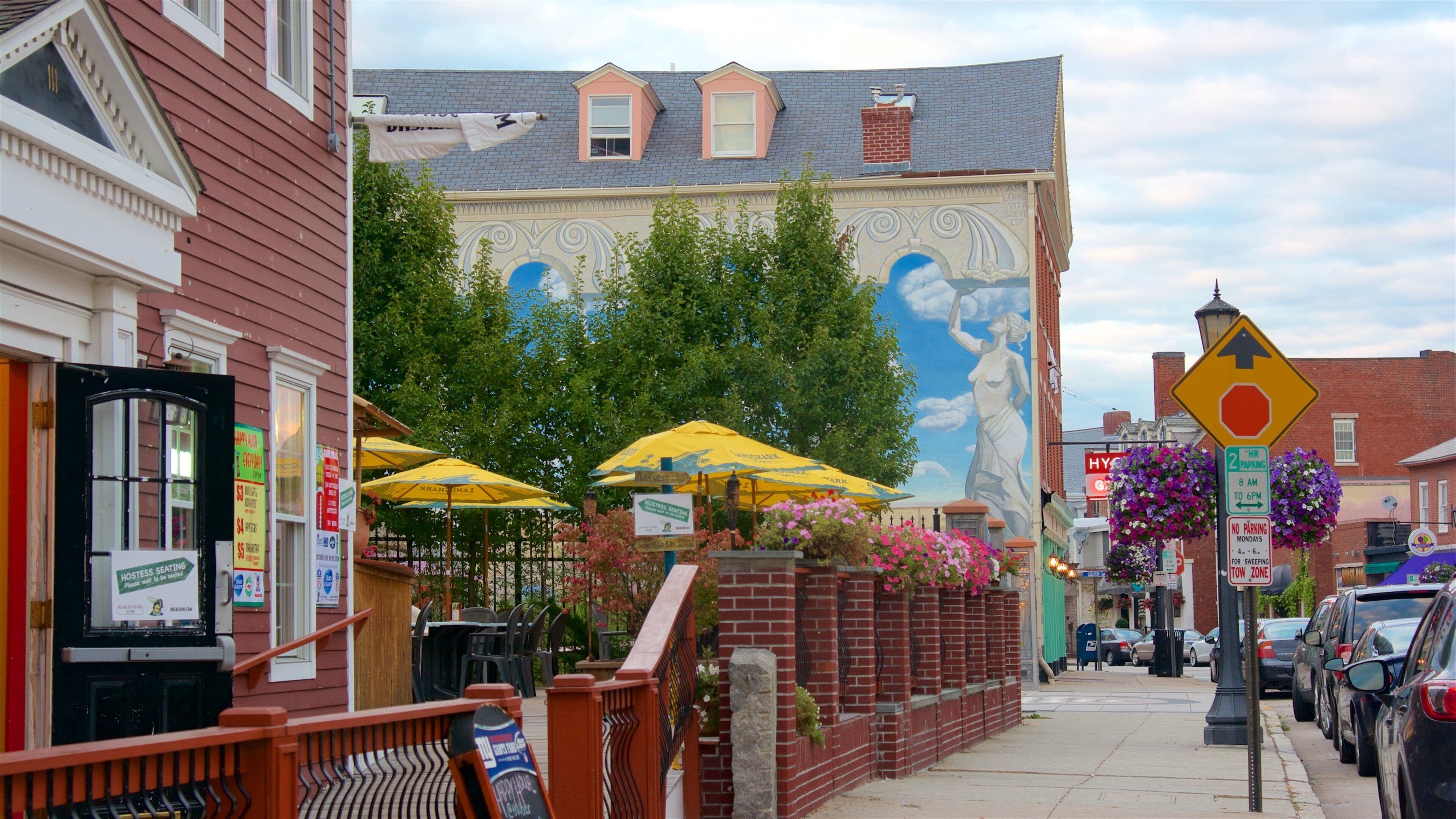 A street with a mural, outdoor seating, and parked cars.