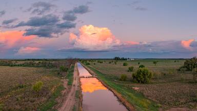 Aerial view of colourful storm clouds at twilight reflected in the water of an irrigation channel
