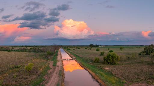 Aerial view of colourful storm clouds at twilight reflected in the water of an irrigation channel