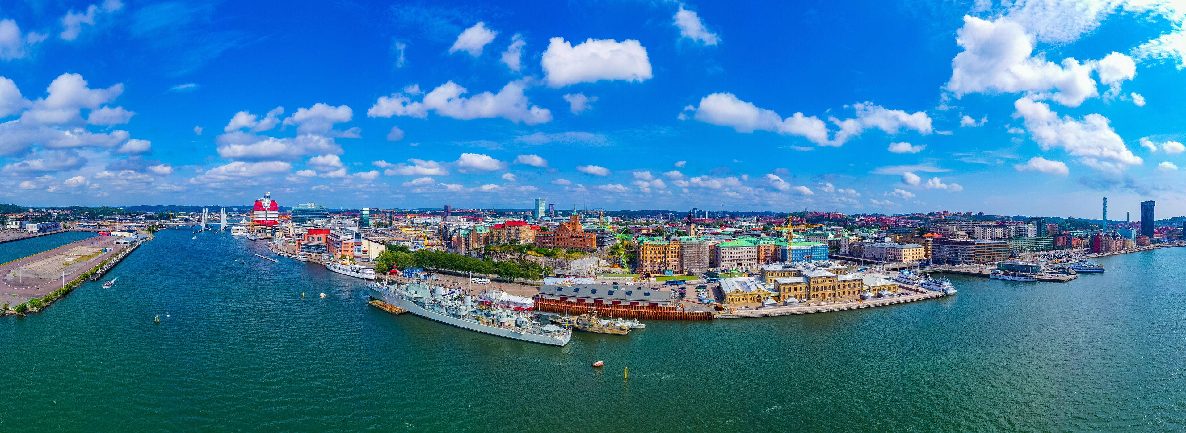A coastal cityscape with a prominent bridge, a large ship docked at a pier, and a mix of historic and modern buildings.