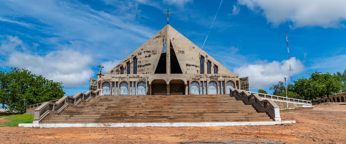 A large, triangular building with a cross on top, surrounded by a white fence and steps leading up to it.