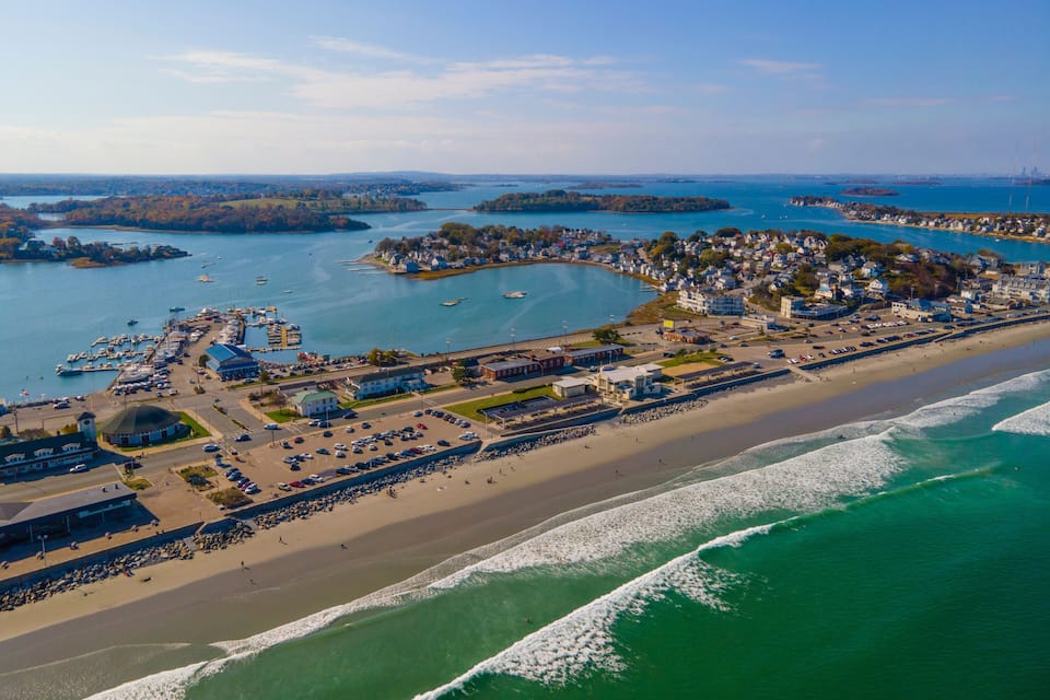 An aerial view of a coastal town with a marina, beach, and surrounding islands.