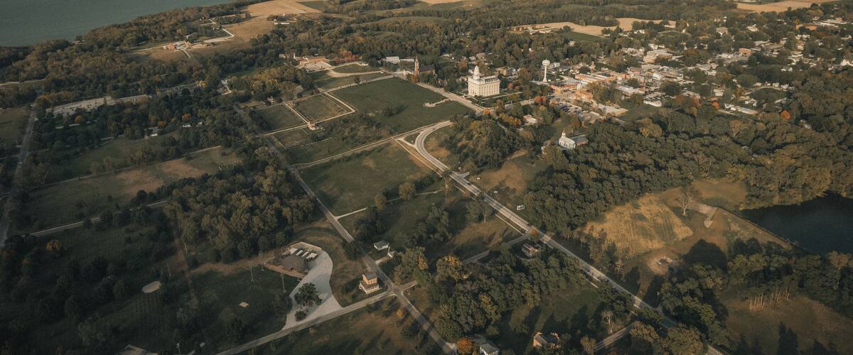 An aerial view of a town with a large white building, surrounded by fields and a river.