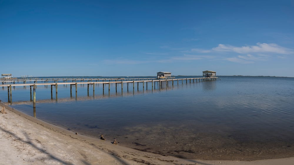 Private docks with boat lifts against the blue sky background at Navarre, Florida. Views of dock from a shore with sand and grasses at the front.
