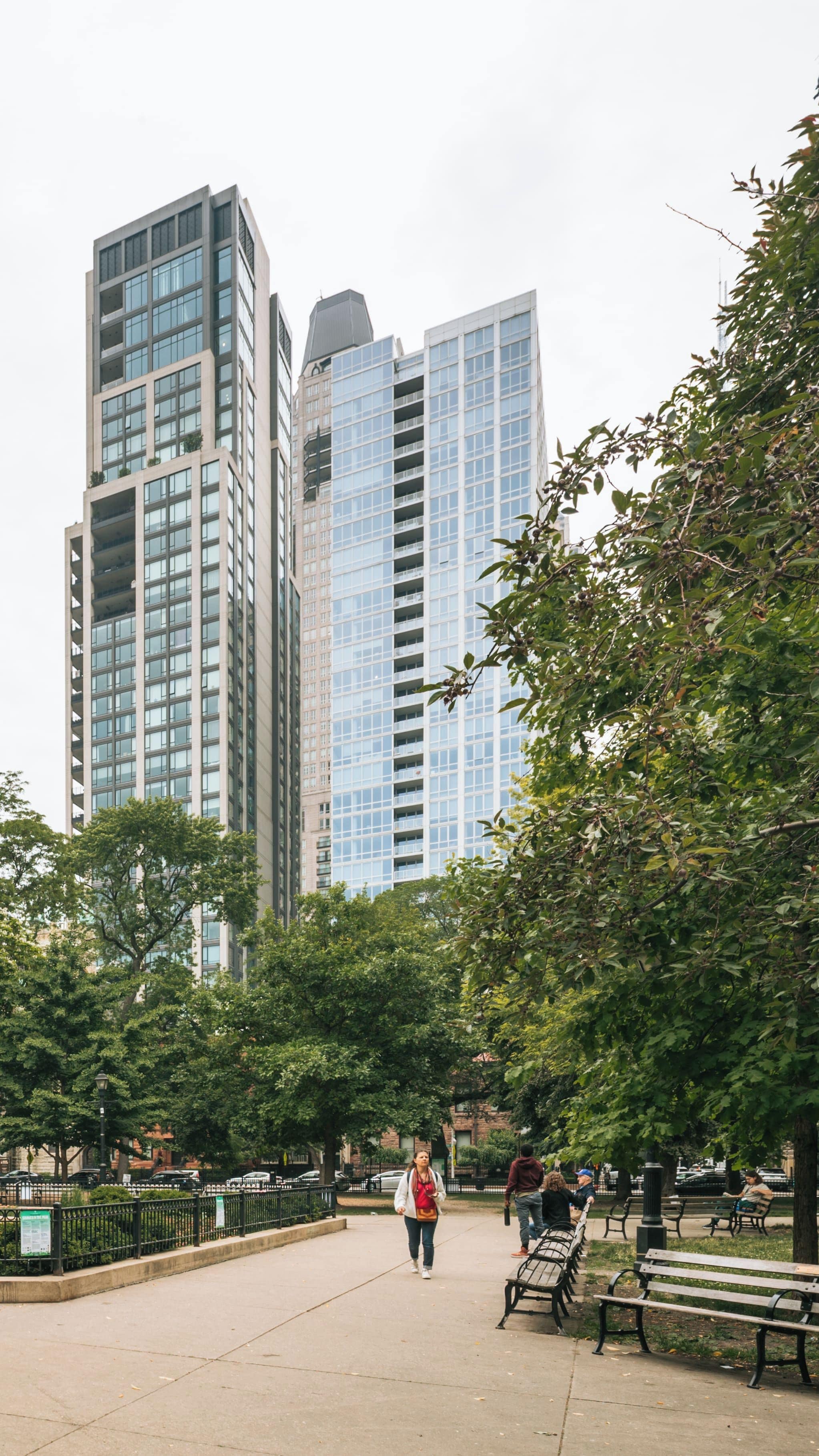 A park with a walking path, benches, and tall buildings in the background.