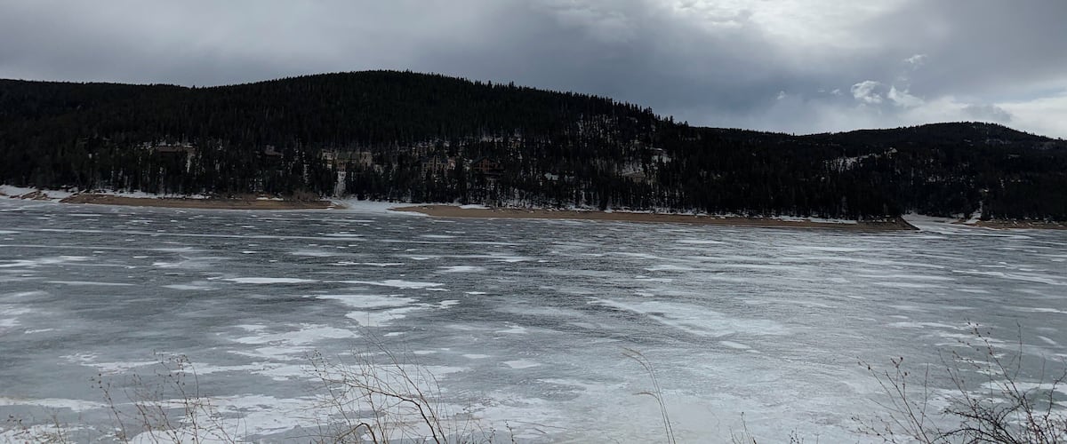 A frozen lake with a forested hill in the background.