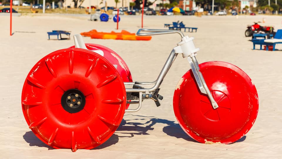 A red inflatable raft on a sandy beach with blue chairs and umbrellas in the background.