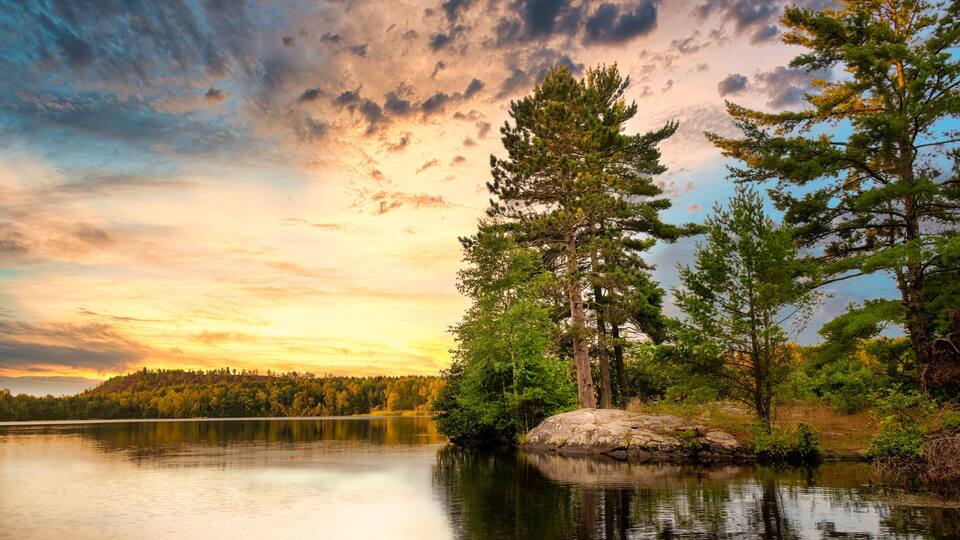 A calm lake with a forested shoreline and a sunset sky.