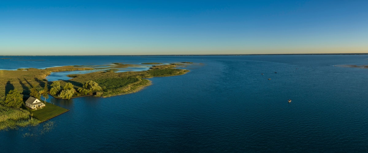 A coastal landscape with a house on a small island, surrounded by water and greenery.
