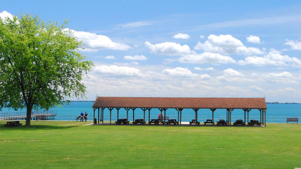 A covered picnic area with benches and picnic tables by a lake.