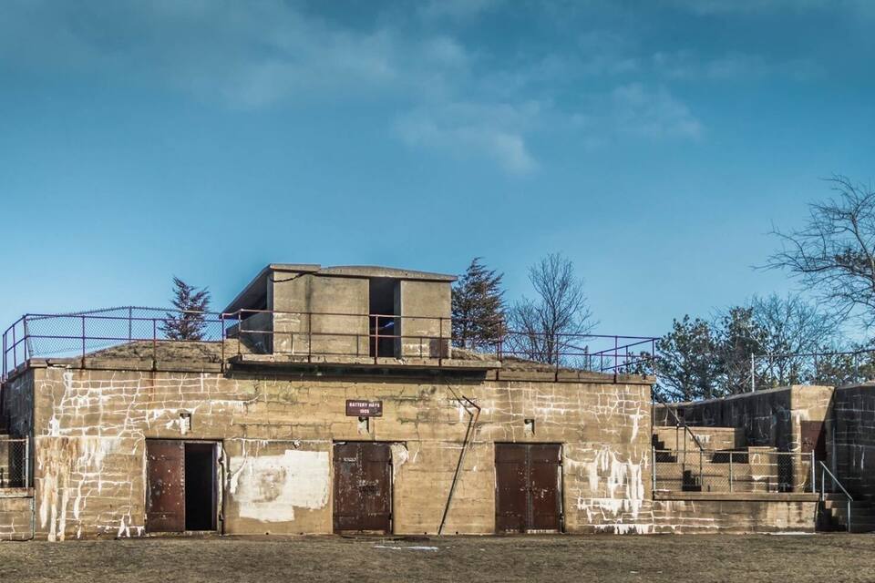 An old, weathered building with a large chimney, a small tower, and a sign that reads "Battery Huts 1905".