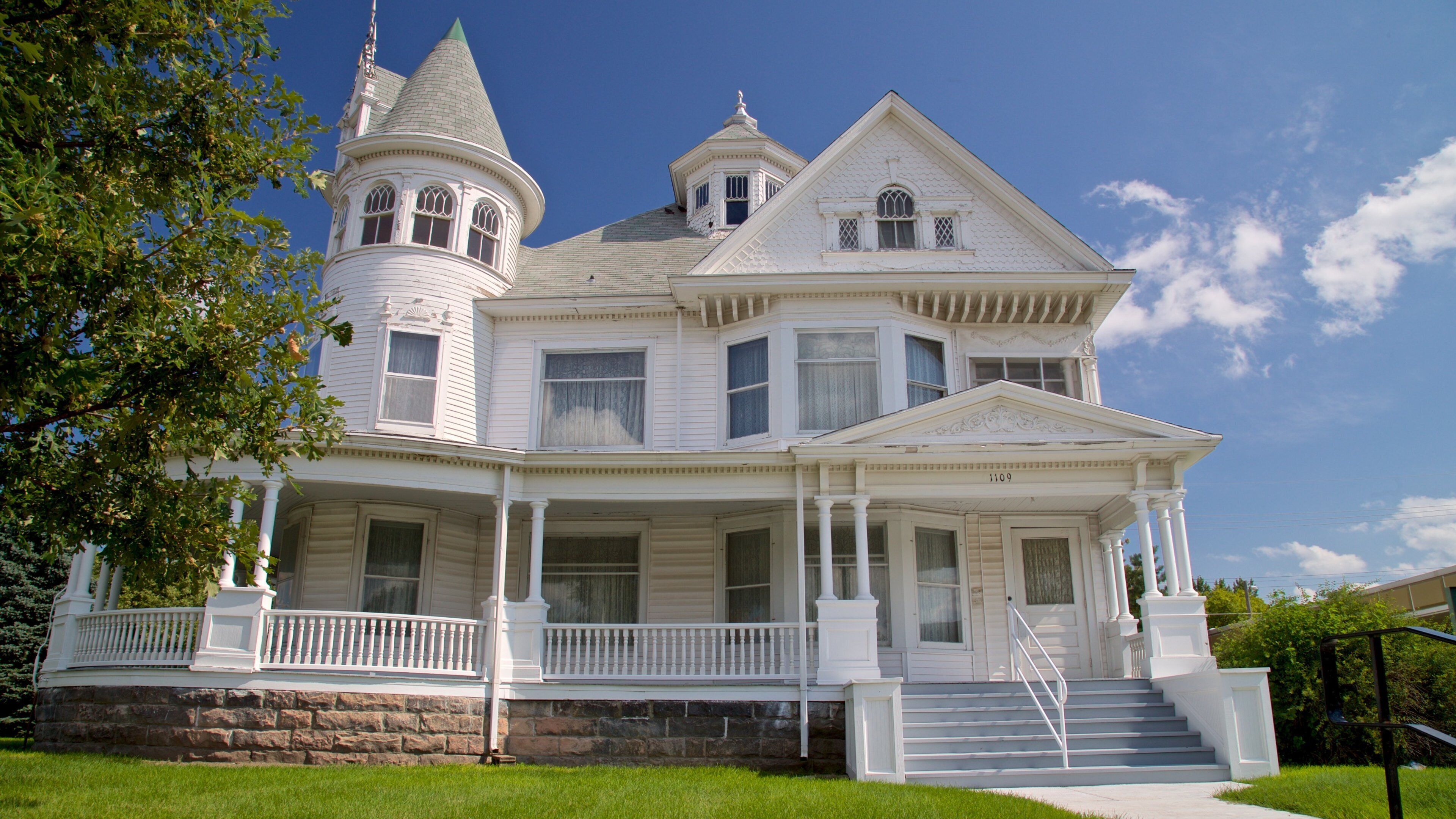 A large white Victorian-style house with a tower, a wrap-around porch, and a stone foundation.