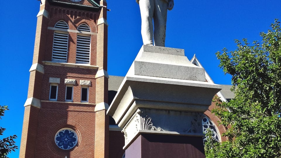 A church with a clock tower and a statue of a man with a hat.