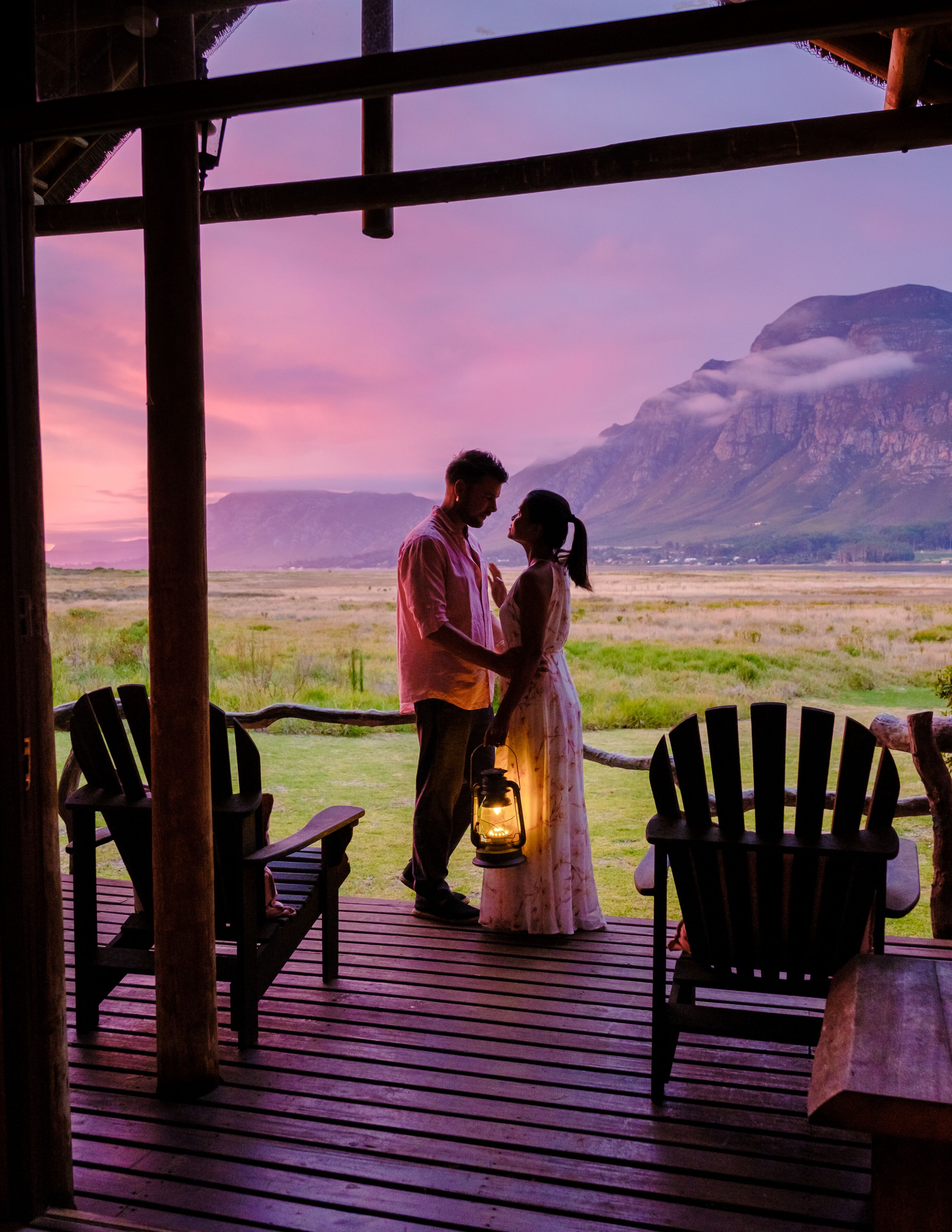 Una pareja en una cubierta de madera contemplando un paisaje extenso con montañas a lo lejos.
