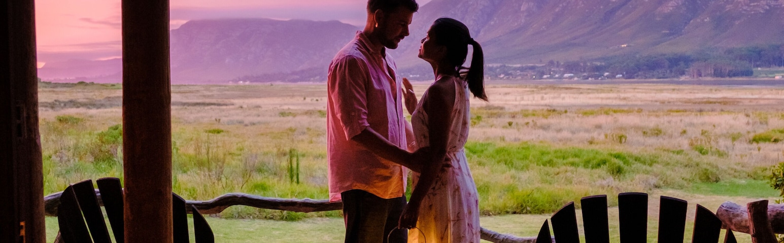 Una pareja en una cubierta de madera contemplando un paisaje extenso con montañas a lo lejos.