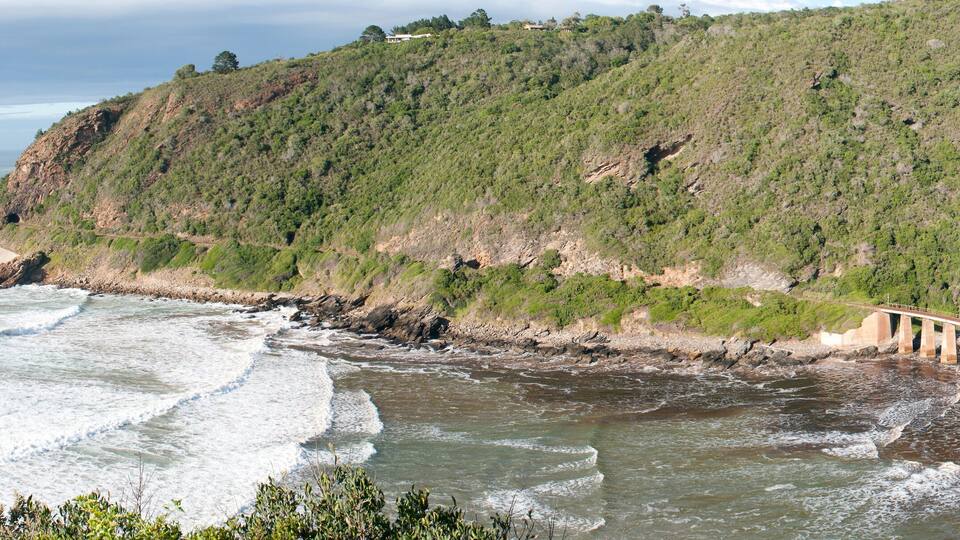 A coastal landscape with a bridge over a river, surrounded by hills and ocean waves.