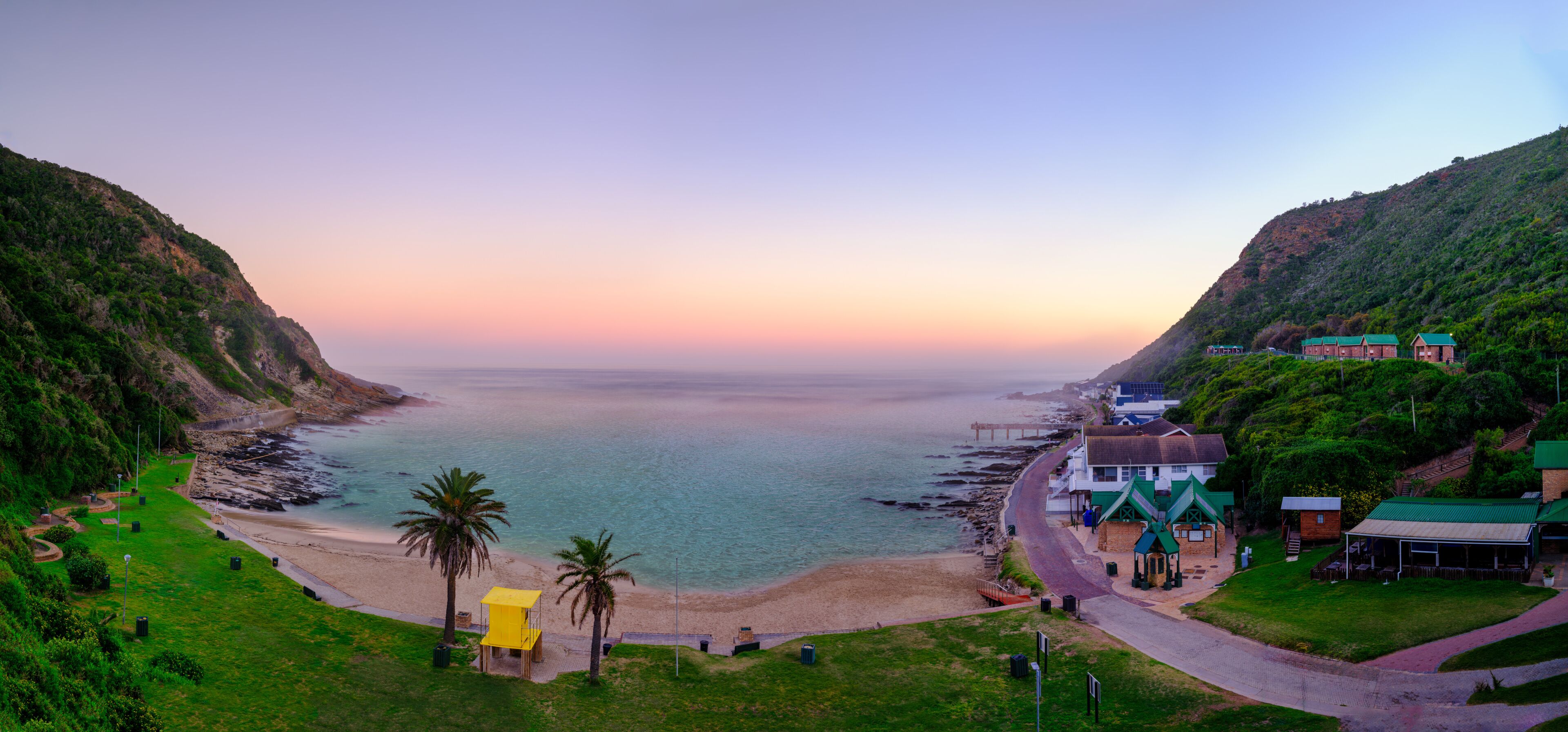 A coastal landscape with a beach, palm trees, and buildings along the shore.