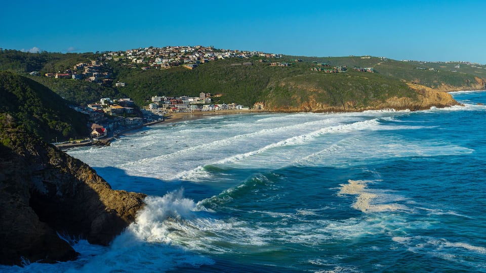 A coastal town with waves crashing against rocky cliffs and a hillside settlement.