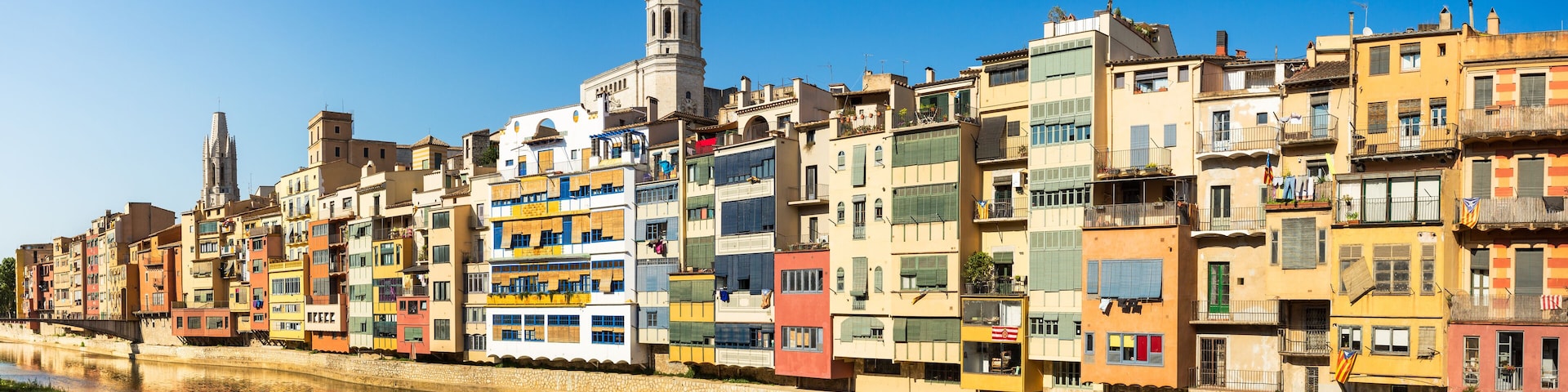 A row of colorful buildings along a river, with a prominent church tower in the background.