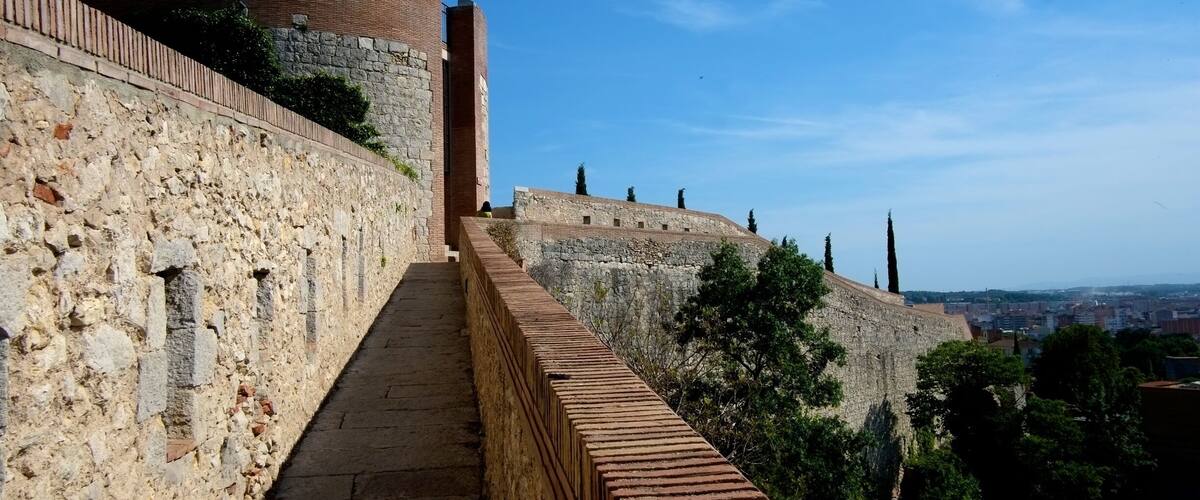 A stone pathway leading up a hill with a brick wall and a round tower.