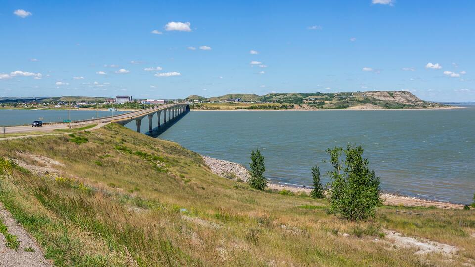 A bridge over a river, grassy hills, and a distant building.
