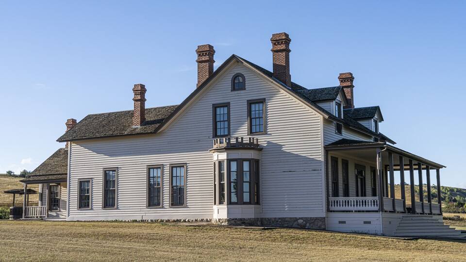 A large white house with multiple chimneys, a covered porch, and a stone foundation.