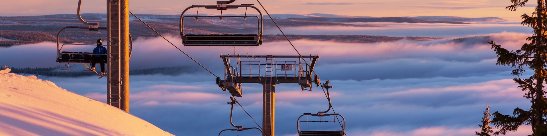 A ski lift with chairs and a snowy mountain landscape.