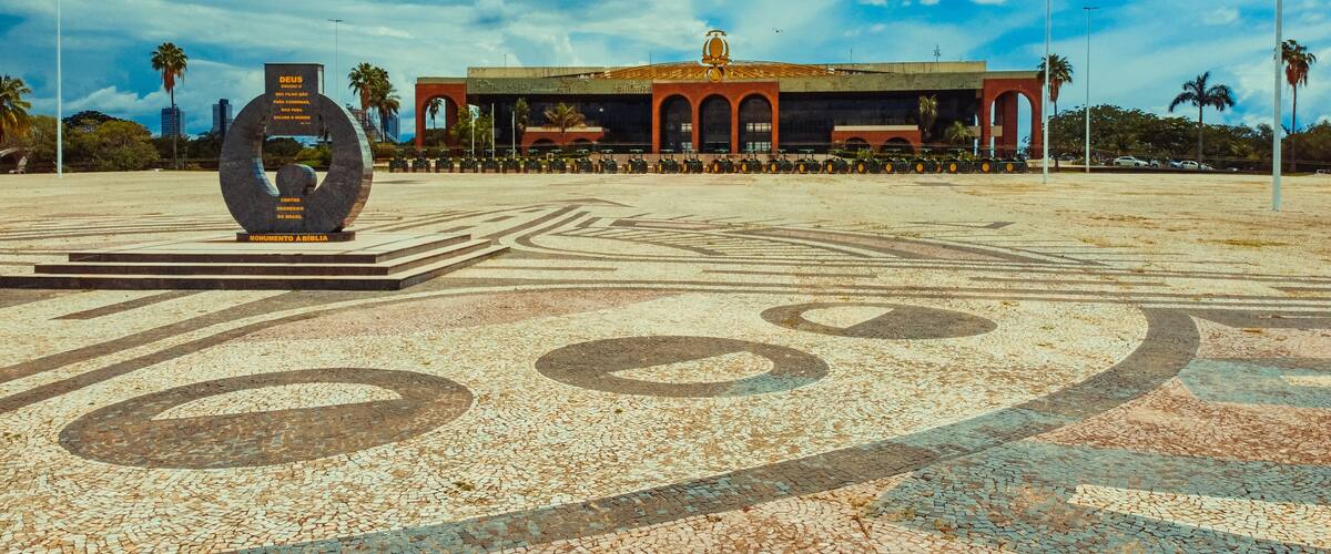 A plaza with a large sculpture, a building with a red roof, and palm trees.