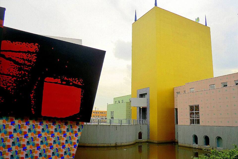 Um edifício moderno com fachada amarela e uma estrutura vermelha grande em primeiro plano.