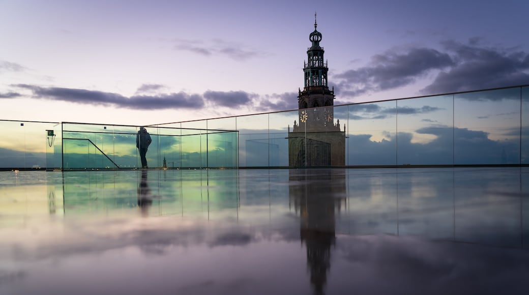 Een persoon loopt over een reflecterend oppervlak, met een historische toren op de achtergrond.