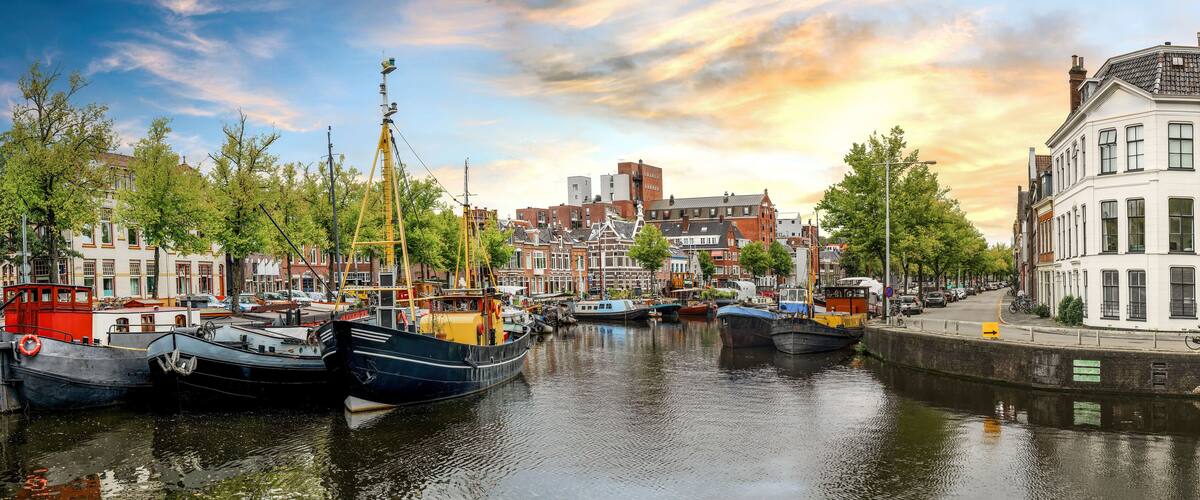 A canal with boats docked, surrounded by historic buildings and trees.