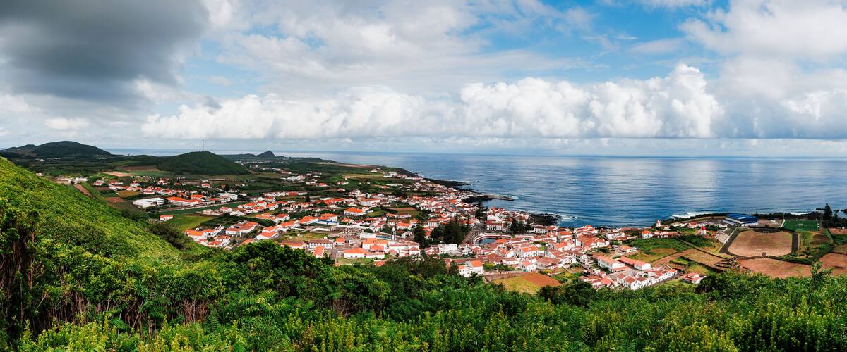 A coastal town with red-roofed houses, green hills, and a view of the ocean.