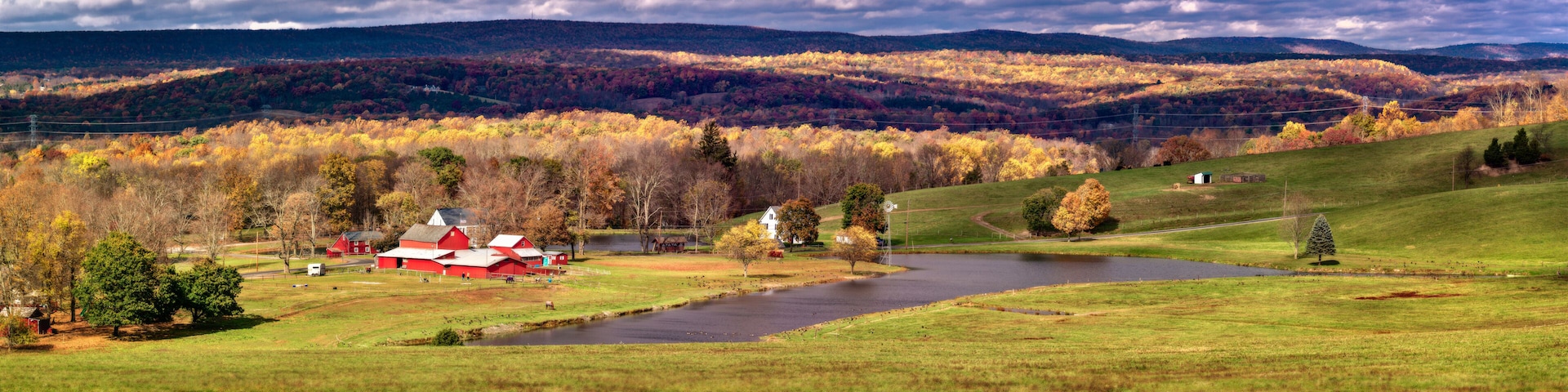 A rural landscape with a river, red barns, and autumn foliage.