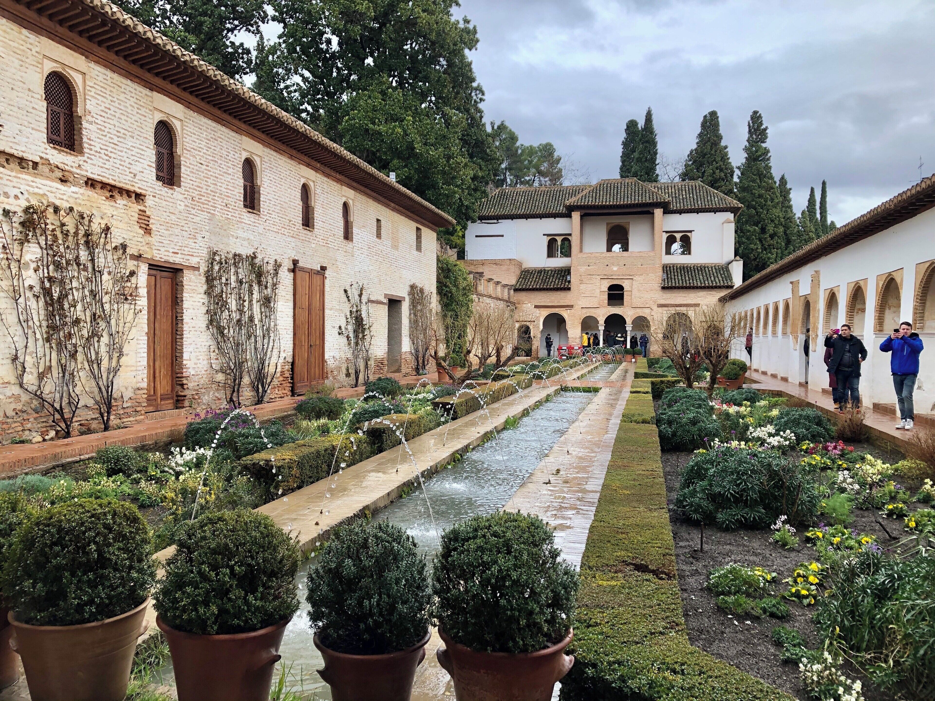 A historic courtyard with a water channel, potted plants, and traditional architecture.