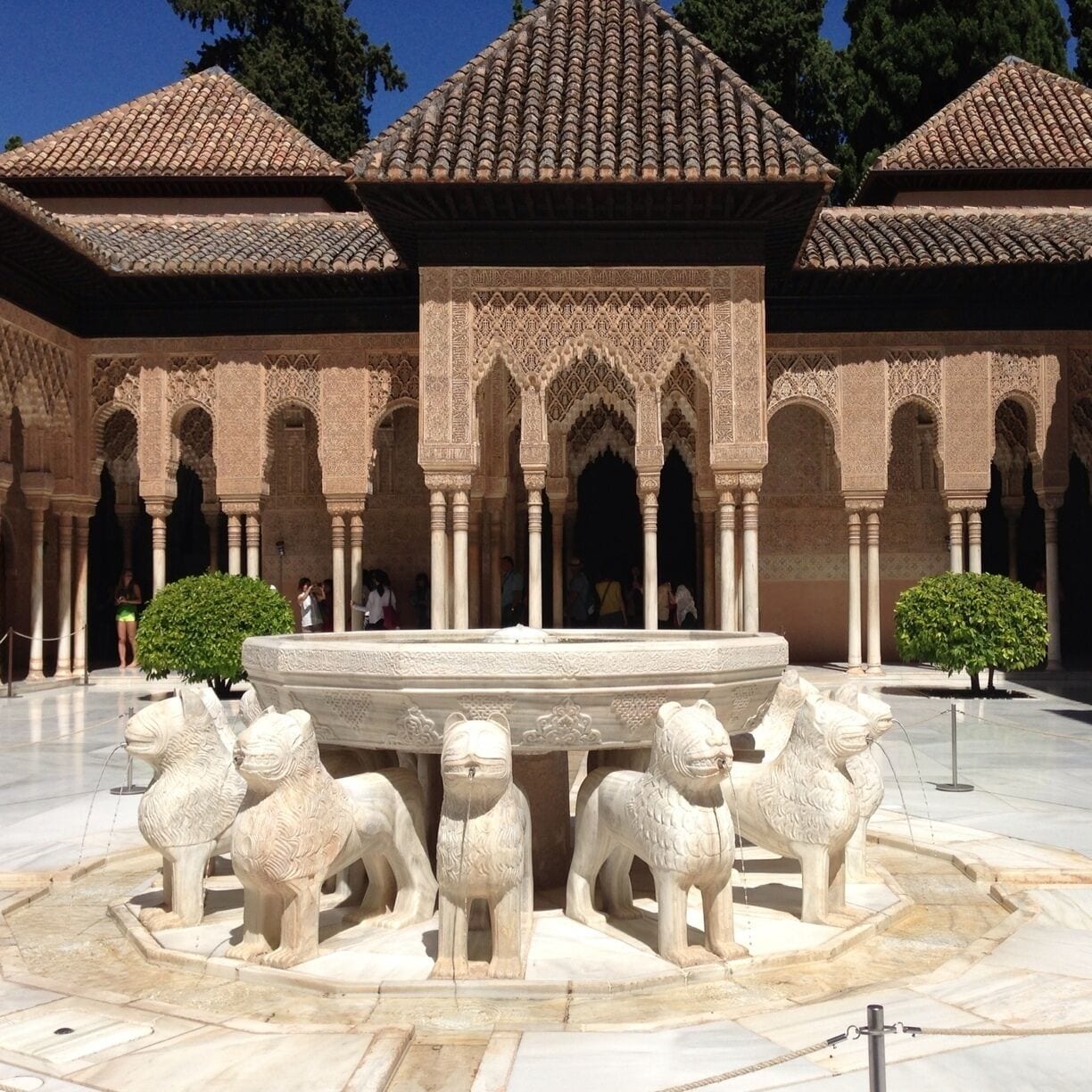 Un patio con arcos decorativos, una fuente y estatuas de leones.