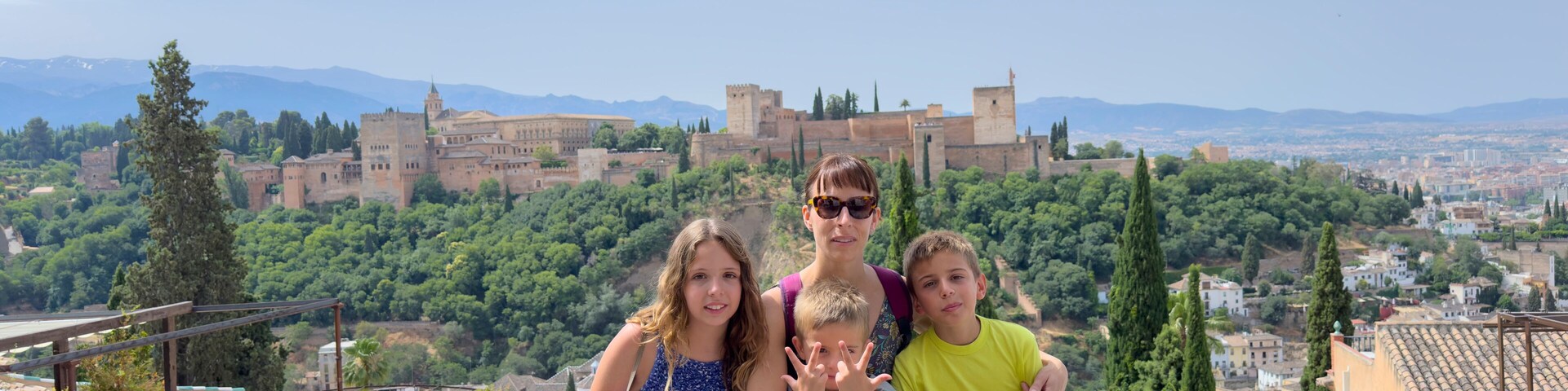 Un grupo de personas sentadas sobre un muro de piedra con vistas a una ciudad histórica, donde se distingue un castillo imponente al fondo.