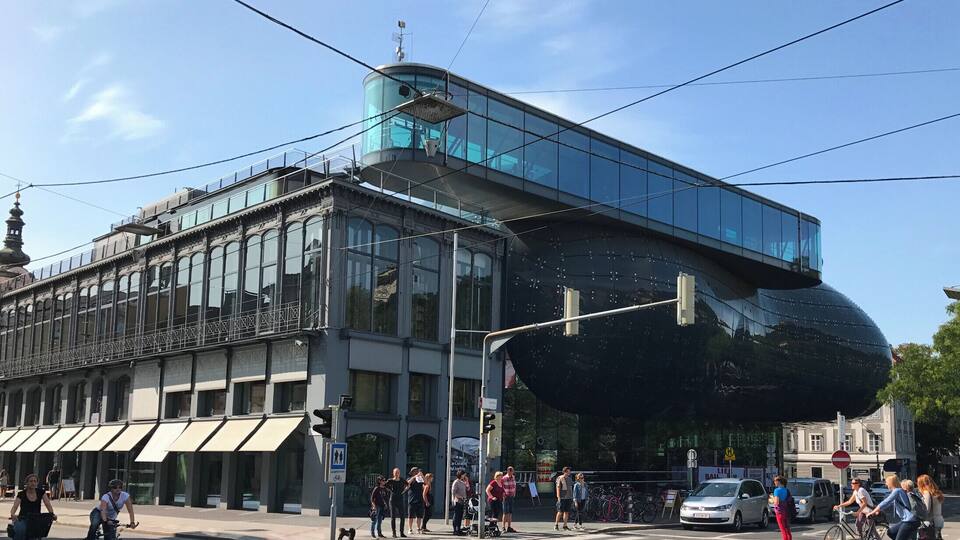 Ein modernes Gebäude mit großen Glasfenstern und einer markanten, kugelförmigen Struktur auf der rechten Seite.