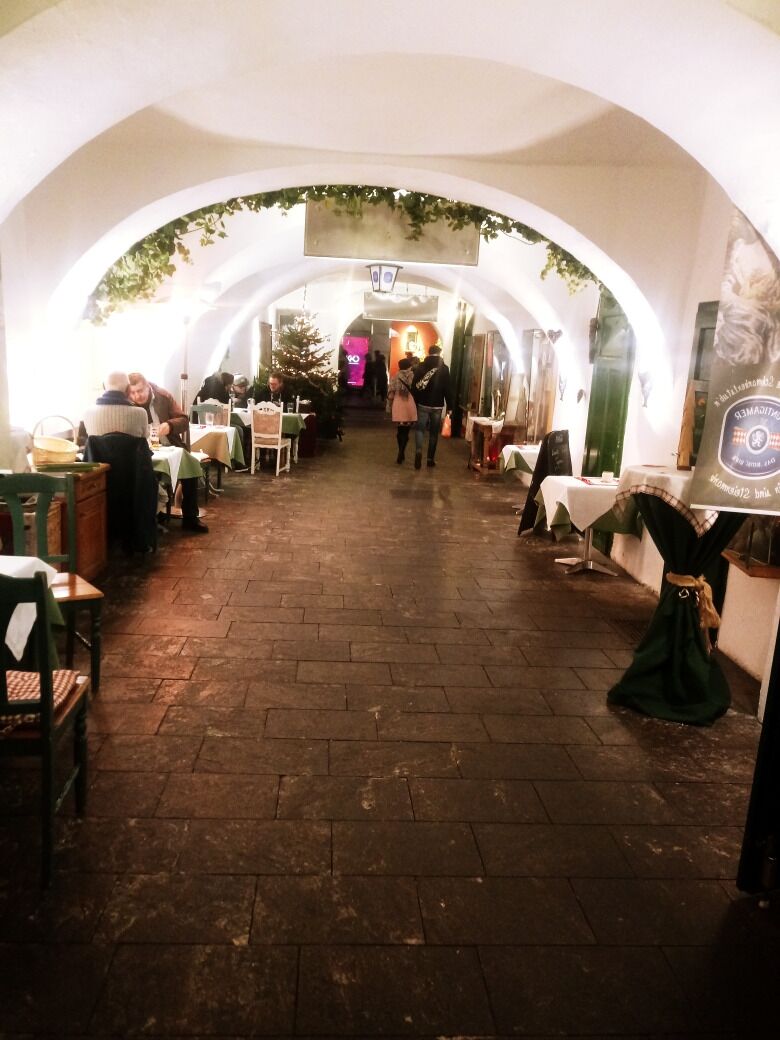An indoor corridor with tables and chairs, arches, and a green plant hanging from the ceiling.