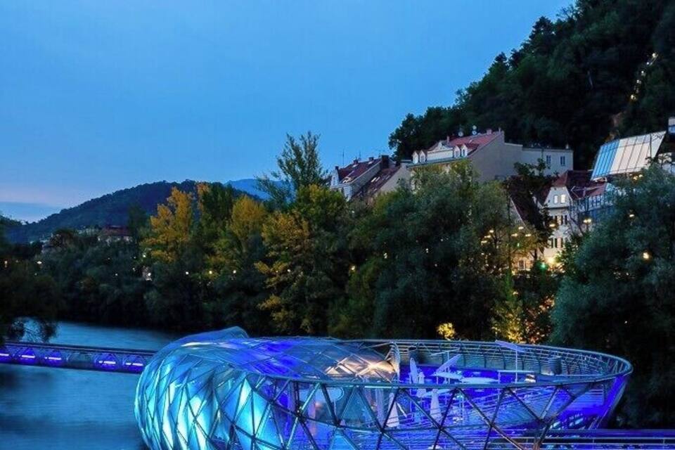 A modern glass structure by a river at dusk.