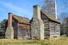 A rustic log cabin with a stone chimney and a wooden barn.