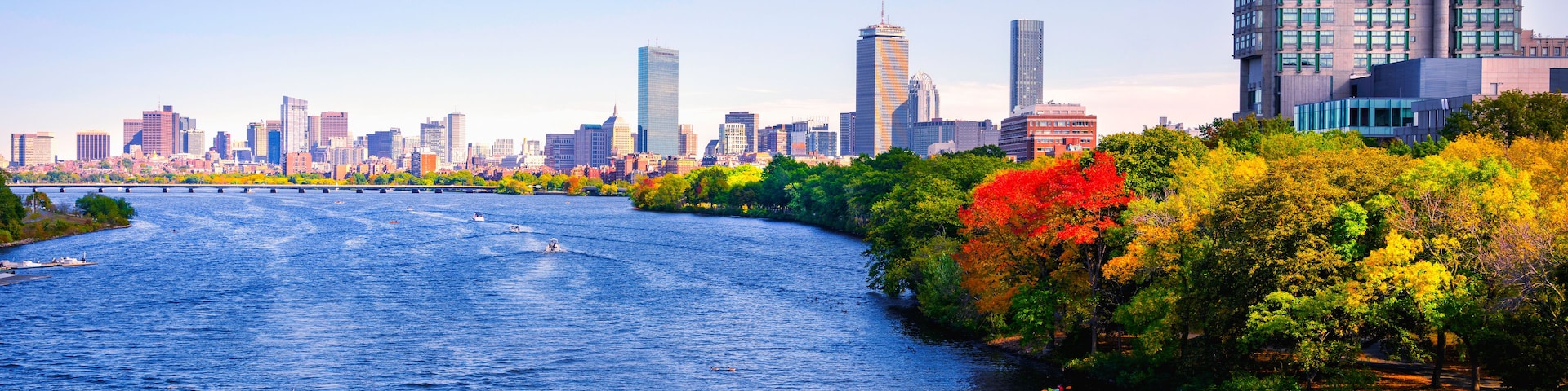 Ein Fluss mit Booten, eine Skyline der Stadt und herbstlich gefärbte Bäume.